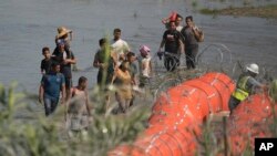 FILE - Migrants trying to enter the US from Mexico approach the site where workers are assembling large buoys to be used as a border barrier along the banks of the Rio Grande in Eagle Pass, Texas, July 11, 2023. 