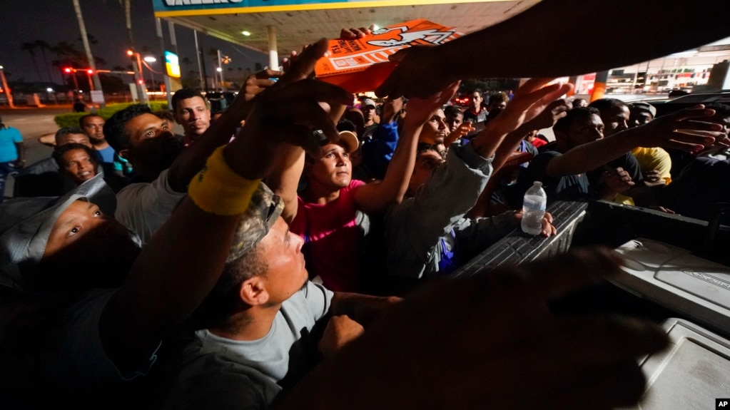 Migrantes reciben pizza de voluntarios después de ser liberados de un centro de descanso en la frontera entre Texas y México, el jueves 11 de mayo de 2023, en Brownsville, Texas. (Foto AP/Julio Cortés)