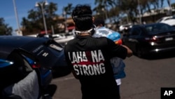 Ken Alba, a Lahaina, Hawaii, resident, carries a bag of ice at a food and supply distribution center set up in the parking lot of a shopping mall in Lahaina, Hawaii, Aug. 17, 2023.