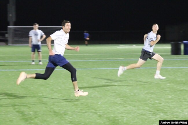 Members of the Carolina Flyers professional men's ultimate frisbee team running and looking up at a frisbee in Chapel Hill, North Carolina on Thursday, April 13, 2023. (VOA/Andrew Smith)