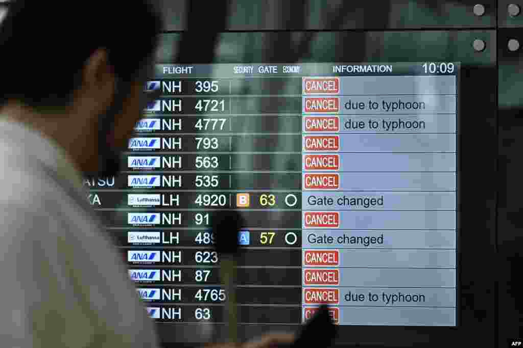 A TV news crew team works in front of a screen showing canceled flights at the departure hall of Tokyo's Haneda Airport as Typhoon Ampil barrels towards Japan's capital.