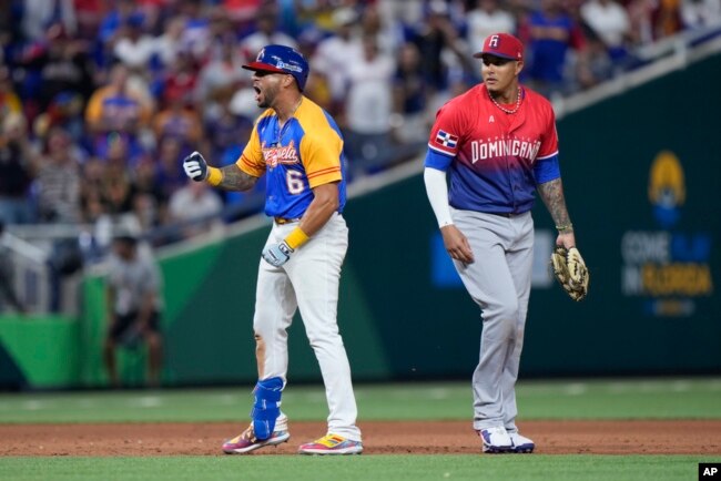 David Peralta (6) de Venezuela celebra después de anotar un doblete de Eugenio Suárez mientras el tercera base de República Dominicana, Manny Machado, observa durante la sexta entrada de un juego del Clásico Mundial de Béisbol, el sábado 11 de marzo de 2023, en Miami. (Foto AP/Wilfredo Lee)