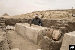 Seorang pekerja barang antik Mesir menyikat alas pembalseman yang baru saja digali di lokasi Piramida Langkah Djoser di Saqqara, 24 kilometer barat daya Kairo, Mesir, 27 Mei 2023. (Foto: AP)