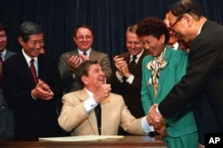 FILE - President Ronald Reagan celebrates with senators and representatives during a signing ceremony in the Old Executive Office Building in Washington on Aug. 10, 1988. Reagan signed into law legislation making moral and financial amends to Japanese Americans kept in U.S. internment camps during World War II.