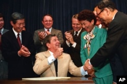 ARCHIVO - El presidente Ronald Reagan celebra con senadores y representantes durante una ceremonia de firma en el Antiguo Edificio de la Oficina Ejecutiva en Washington el 10 de agosto de 1988. Reagan promulgó una legislación que hace enmiendas morales y financieras a los japoneses-estadounidenses recluidos en campos de internamiento de EE. Segunda guerra.