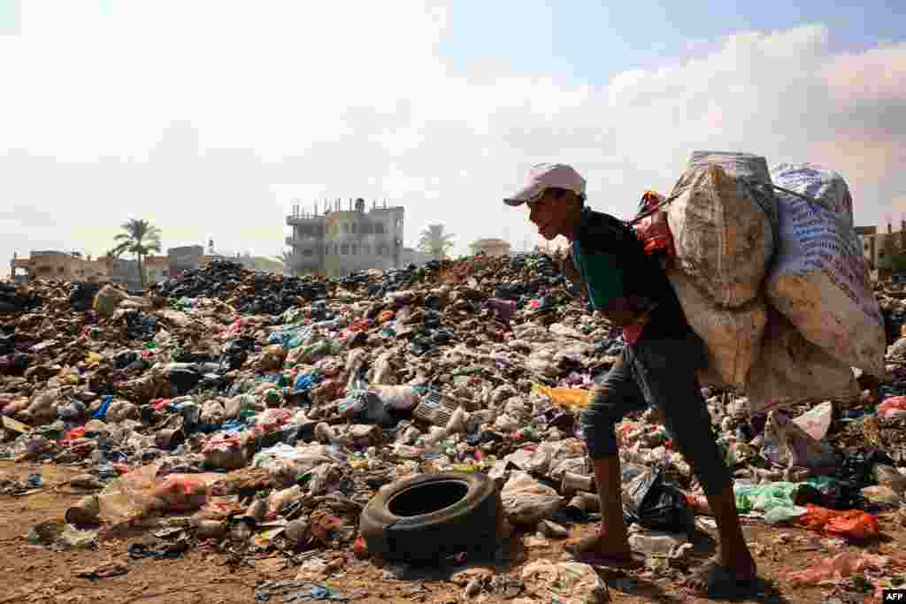 Seorang pemuda Palestina membawa karung berisi barang-barang yang masih bisa diselamatkan berjalan melewati tumpukan sampah saat pengumpulan sampah dan layanan kota lainnya terhenti akibat pemboman Israel, dekat kamp pengungsi Palestina al-Maghazi, di Jalur Gaza tengah. (AFP)&nbsp;