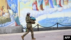 A female Ukrainian serviceman carries flowers in colors of the Ukrainian flag as she walks to take part in the funeral service of a lieutenant colonel killed in battle, at the Mykhaylo Gold Domes Cathedral in Kyiv on Feb. 27, 2023.