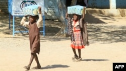 FILE - Children carry packs of humanitarian aid at a school housing displaced Sudanese who had fled violence in their war-torn country, near Gedaref, March 10, 2024. The majority of those fleeing the war in Sudan are under age 18.