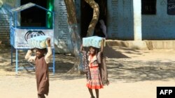 FILE—Children carry packs of humanitarian aid at a school housing displaced Sudanese who had fled violence in their war-torn country, near Gedaref, March 10, 2024.