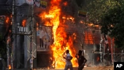 Dua orang pria berlarian melewati pusat perbelanjaan yang dibakar oleh para pengunjuk rasa dalam aksi menentang Perdana Menteri Sheikh Hasina dan pemerintahannya di Dhaka, Bangladesh, Minggu, 4 Agustus 2024. (Rajib Dhar/AP)