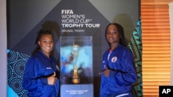 FILE: Haitian goalkeeper Kerly Theus, left, and fellow teammate Esthericove Joseph, pose for a photo alongside the Women’s World Cup trophy during a ceremony as part of its global tour, in Port-au-Prince, Haiti, Saturday, April 15, 2023. 