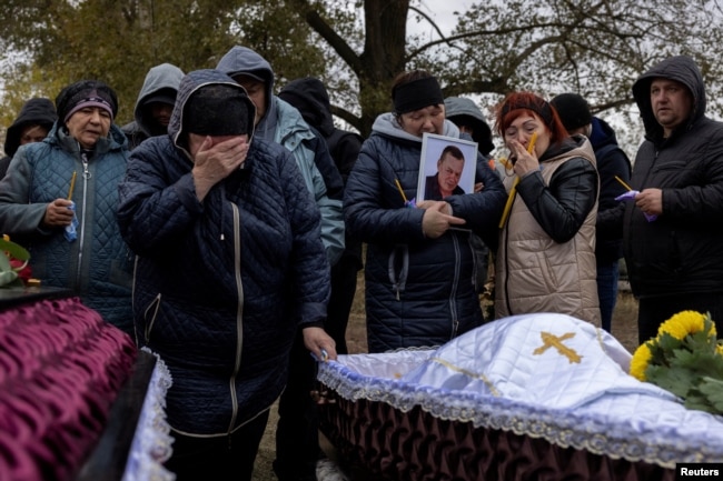 Relatives mourn at the coffins of Iryna Kharbaka and Oleksandr Khodak, who were killed in a Russian missile attack, amid Russia's ongoing invasion of Ukraine, at the village cemetery, in the village of Hroza, near Kharkiv, Ukraine, Oct. 9, 2023.