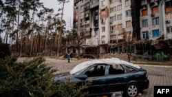 A woman walks past a residential building at the Irpinsky Lipky residential complex, which was heavily damaged during fighting between Russian and Ukrainian troops in the town of Irpin, near Kyiv, Feb. 16, 2023.