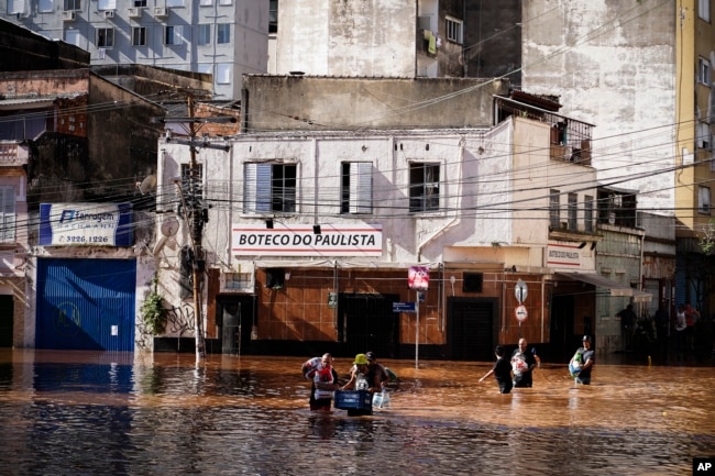 People wade through an area flooded by heavy rains in Porto Alegre, Rio Grande do Sul state, Brazil, Monday, May 6, 2024. (AP Photo/Carlos Macedo)