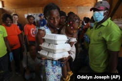 A woman with a child walks away with food from the World Food Programme (WFP) in Port-au-Prince, Haiti, Thursday, July 25, 2024. (AP Photo/Odelyn Joseph)