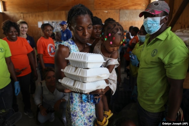 A woman carrying a child walks away with food from the World Food Program (WFP) in Port-au-Prince, Haiti, Thursday, July 25, 2024. (AP Photo/Odelyn Joseph)