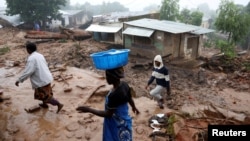 FILE - People walk past houses damaged by Cyclone Freddy in Chilobwe, Blantyre, Malawi, March 17, 2023.