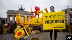A Greenpeace activist poses in front of a mock-up dinosaur in front of the Brandenburg Gate marking the nuclear shutdown in Germany in Berlin, Germany, April 15, 2023.