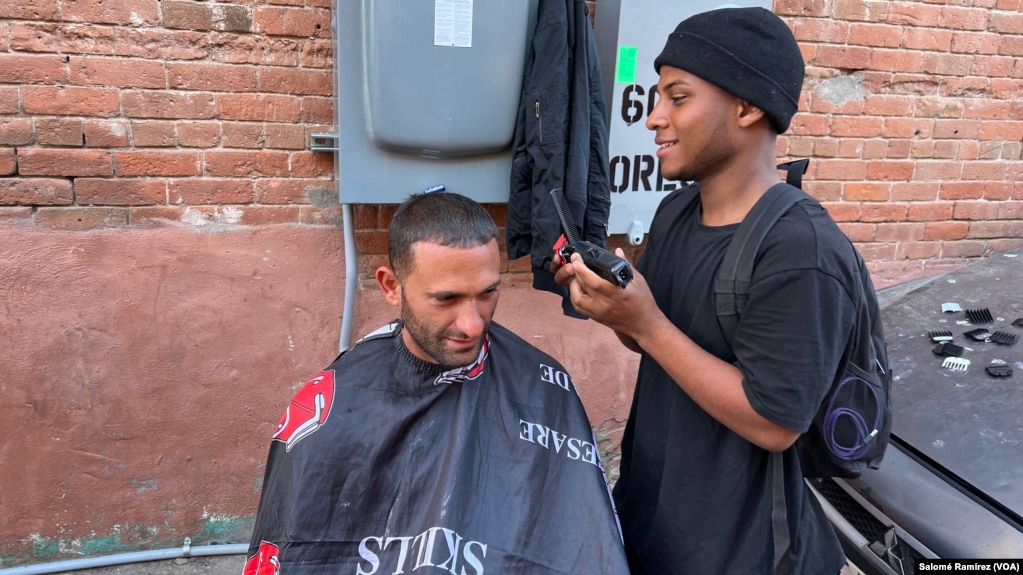 Un migrante venezolano de 19 años ofrece servicios de barbería por 10 dólares a otro migrante cubano en un campamento improvisado en el centro de la ciudad de El Paso, Texas, el 8 de mayo de 2023.