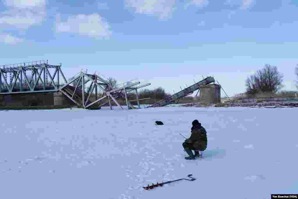 A fisherman ignores the sound of the explosions from what seems artillery fire and instead tries to catch a fish at this frozen river in Kupiansk, Feb. 17, 2023.