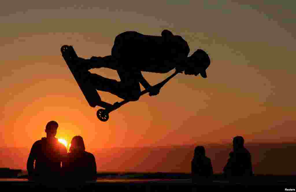 A young man performs a trick on a scooter during the sunset at a skate park on the sea wall of Calais, France, Aug. 15, 2023. 