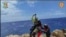 In this picture taken from video distributed on Aug. 6, 2023 by the Italian Alpine Rescue squads, a migrant stranded on a rocky reef on the tiny Italian southern island of Lampedusa is pluck to safety by helicopter.  (Italian Alpine Rescue via AP)