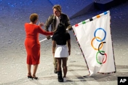 Tom Cruise, right, is handed over the Olympic flag from Los Angeles Mayor Karen Bass, left, during the 2024 Summer Olympics closing ceremony at the Stade de France, Aug. 11, 2024, in Saint-Denis, France