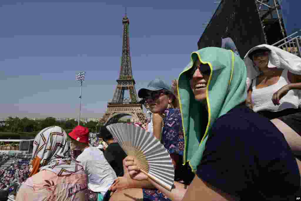 Stephanie Touissaint, foreground, uses a fan to keep cool in the sweltering heat at Eiffel Tower Stadium during a beach volleyball match between Cuba and Brazil at the 2024 Summer Olympics, in Paris, France.