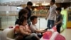 在上海一家商场里一名女子抱着一个小女孩带着一个小男孩驾驶玩具汽车。（2021年6月1日）