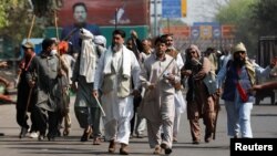 Supporters of former Pakistani Prime Minister Imran Khan carry sticks as they walk towards Khan's house, in Lahore, Pakistan, March 16, 2023. A poster of Khan is seen in the background.