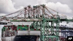 FILE - A sailboat passes a cargo ship unloading containers the port of Los Angeles in San Pedro, June 15, 2023.