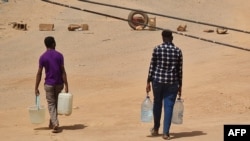 2023年5月25日，喀土穆两名苏丹男子双手拎着各种装满清水的容器往家里走去。