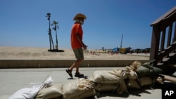 Tom Ostrom passa por uma casa protegida com sacos de areia em Seal Beach, Califórnia, a 18 de agosto de 2023. O furacão Hilary está a passar ao largo da costa mexicana do Pacífico como uma poderosa tempestade de categoria 4, ameaçando desencadear chuvas torrenciais.