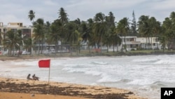 Tourists sit on La Pared beach as Tropical Storm Ernesto passes by Luquillo, Puerto Rico, Aug. 13, 2024.