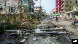 Warga melintasi jalan yang dipenuhi oleh tiang lampu dan pohon yang tumbang pasca Topan Mocha di kotapraja Sittwe, Rakhine State, Myanmar, Senin, 15 Mei 2023. (Foto: AP)