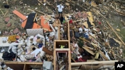 Un hombre, arriba en el centro, rescata una chaqueta mientras observa una casa dañada por un tornado, el domingo 26 de marzo de 2023, en Rolling Fork, Mississippi.