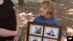 Olive Wilson shows off her family photos as she plays at a park on June 14, 2024. 