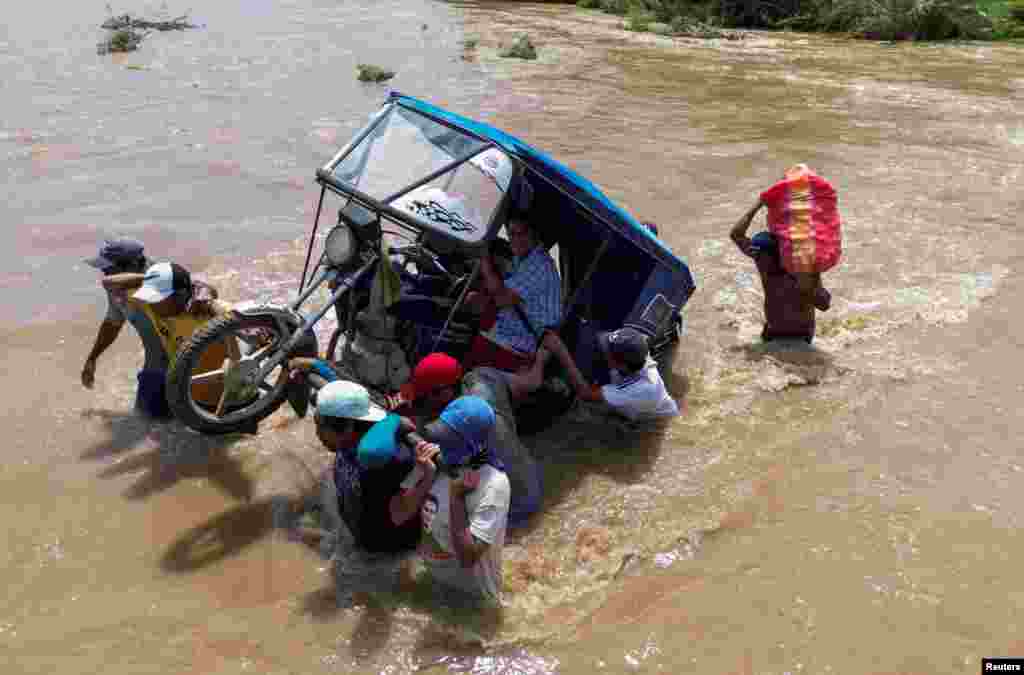 Residents carry a motorcycle taxi through a stream flooded by rains caused by the direct influence of Cyclone Yaku, in Piura, Peru, March 11, 2023. 