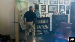 In this image taken through an office window, a law enforcement officer surveys the office of Representative Gerry Connelly in Fairfax, Va., May 15, 2023, after police say a man wielding a baseball bat attacked two Connolly staffers.