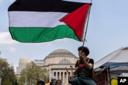 A student protester waves a large Palestinian flag at an encampment on the Columbia University campus, April 29, 2024, in New York. Critics of the war in Gaza have defied a deadline at Columbia to disband.