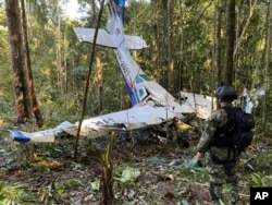 In this photo released by Colombia's Armed Forces Press Office, a soldier stands in front of the wreckage of a Cessna C206, May 18, 2023, that crashed in the jungle of Solano in the Caqueta state of Colombia.