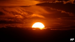 FILE - The setting sun illuminates the clouds over the Rocky Mountains after a third straight day of record-breaking heat Sunday, July 14, 2024, in Denver. (AP Photo/David Zalubowski)