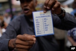 A man explains how to vote while holding up an unmarked ballot as he opens a polling station for the opposition's primary presidential election at Luis Brion square in Caracas, Venezuela, Oct. 22, 2023.