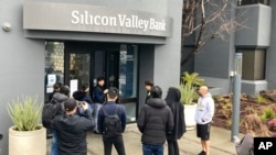 A person standing in an entrance of a Silicon Valley Bank, middle rear, talks to people waiting outside the bank in Santa Clara, California, March 10, 2023.