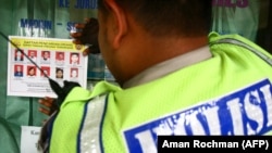 Seorang polisi menempelkan stiker daftar pencarian orang untuk tersangka teroris di sebuah kaca jendela di Malang, Jawa Timur, 30 September 2011. (Foto: Aman Rochman/AFP)