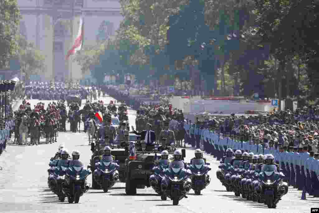 Presiden Prancis Emmanuel Macron melambai di atas mobil komando selama parade militer Hari Bastille di Avenue Foch, dengan Arc de Triomphe di latar belakang, di ibu kota Paris. (AFP)&nbsp;