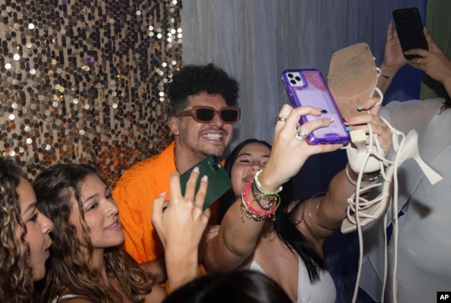 Dr. Pedro Juan Vázquez, better known by his stage name PJ Sin Suela, poses for group selfies at a high school prom in Camuy, Puerto Rico, Thursday, June 6, 2024. (AP Photo/Alejandro Granadillo)