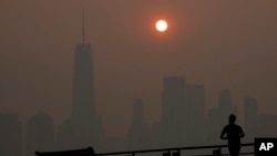 FILE - A man runs in front of the sun rising over the lower Manhattan skyline in Jersey City, NJ, amid the smoke from Canadian wildfires June 8, 2023.