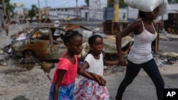 FILE - Girls holding hands are led past a burnt car blocking the street as they evacuate the Delmas 22 neighborhood to escape gang violence in Port-au-Prince, Haiti, May 2, 2024. 