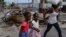 FILE - Girls holding hands are led past a burnt car blocking the street as they evacuate the Delmas 22 neighborhood to escape gang violence in Port-au-Prince, Haiti, May 2, 2024. 